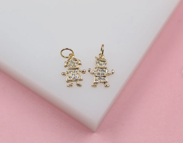 Two gold charms shaped like a boy and a girl, encrusted with sparkling cubic zirconia stones, rest on a white display block.