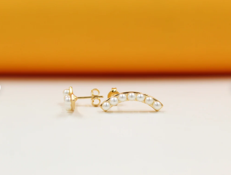A pair of curved gold stud earrings features small white pearls embedded along the arch.