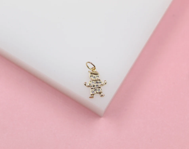 A sparkling gold boy charm encrusted with cubic zirconia stones rests on a white display surface against a pink background.