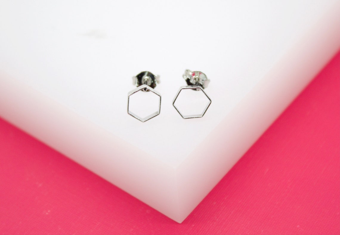 A pair of minimalist silver geometric hexagon stud earrings rest on a white surface.