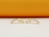 A pair of curved gold stud earrings featuring a row of small white pearls rests against a warm peach-toned background.