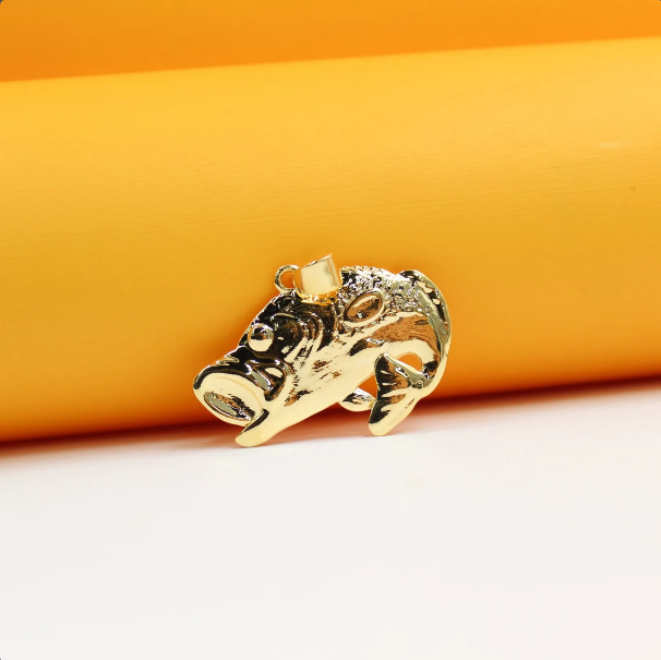 A shiny gold fish pendant rests on a bright orange and white surface.