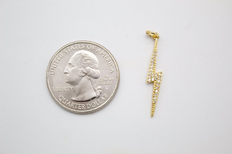 A gold lightning bolt charm rests next to a US quarter coin to show its scale.