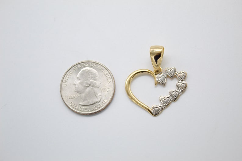 A two-tone gold heart pendant rests next to a US quarter coin for scale on a light background.
