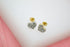A pair of gold heart-shaped stud earrings encrusted with small sparkling diamonds sits on a white display surface.