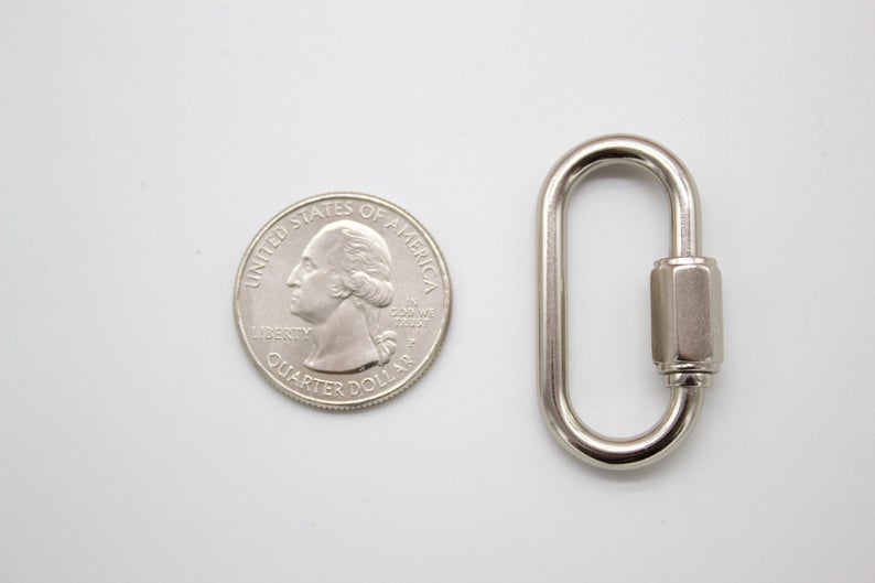 A shiny silver quick link sits next to a US quarter coin on a white surface to show its size.