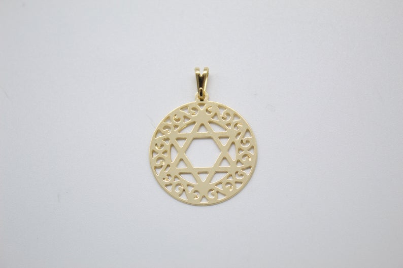 A gold Star of David pendant rests against a plain white background, featuring intricate openwork patterns inside a circular frame.