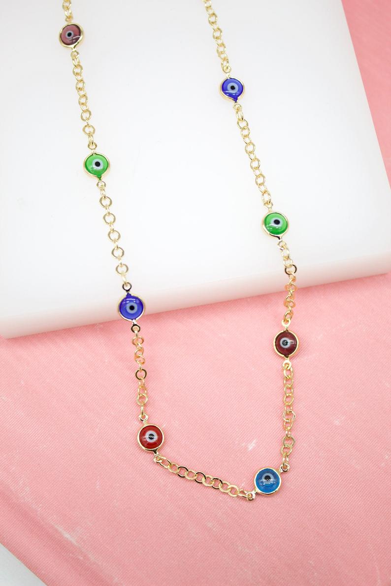 A gold chain necklace displays colorful evil eye charms in blue, green, red, and purple against a pink and white background.