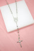 A shiny silver rosary necklace with a crucifix rests on a white display block against a pink background.