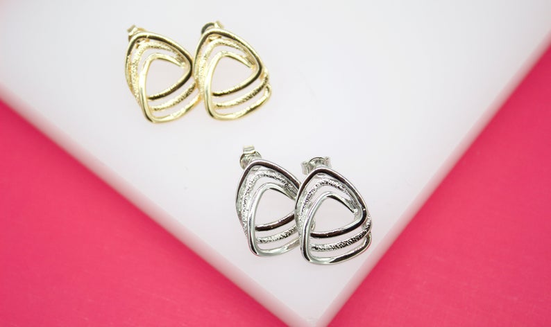 Two pairs of textured, openwork triangle stud earrings display in gleaming gold and silver tones on a white and pink background.