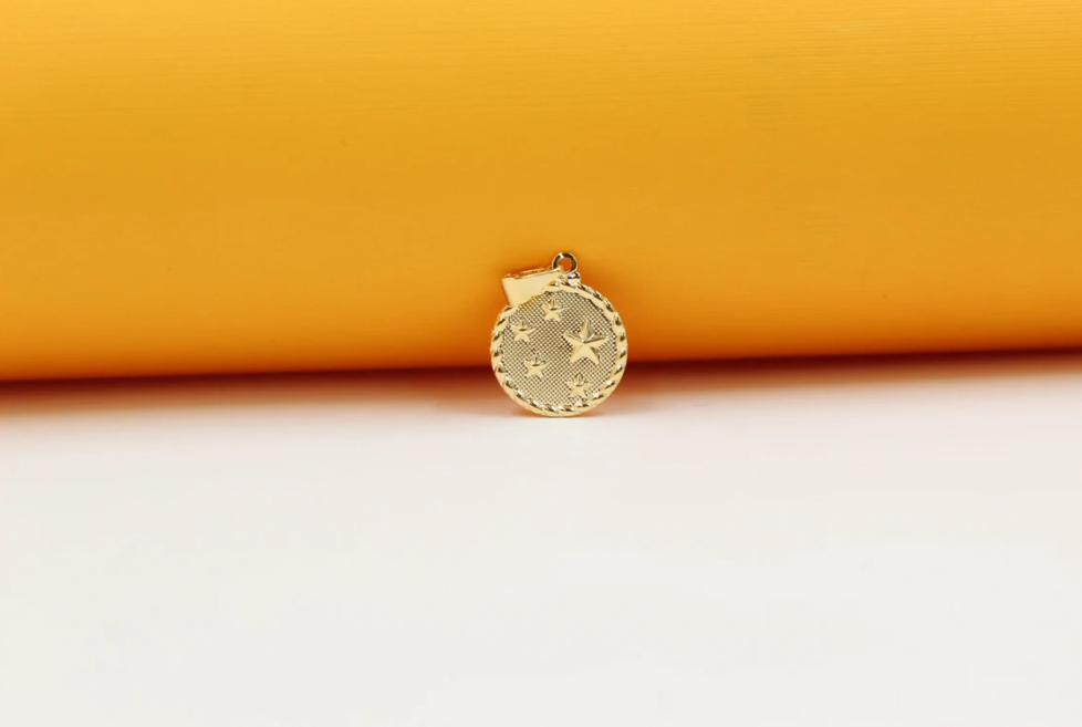 A shiny gold coin pendant featuring embossed star details rests against a vibrant yellow and white background.