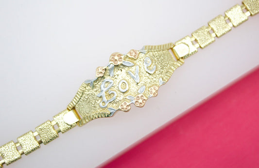 A tri-color gold ID bracelet features the word "LOVE" in raised white gold letters framed by delicate floral accents against a textured gold background.