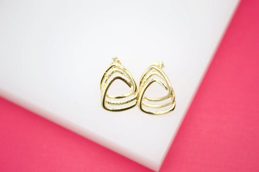 A pair of elegant gold geometric triangle stud earrings rests on a white and pink display stand.
