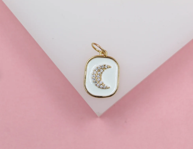 A gold-rimmed rectangular pendant with white enamel features a sparkling crystal-镶bed crescent moon resting against a pink and white geometric background.