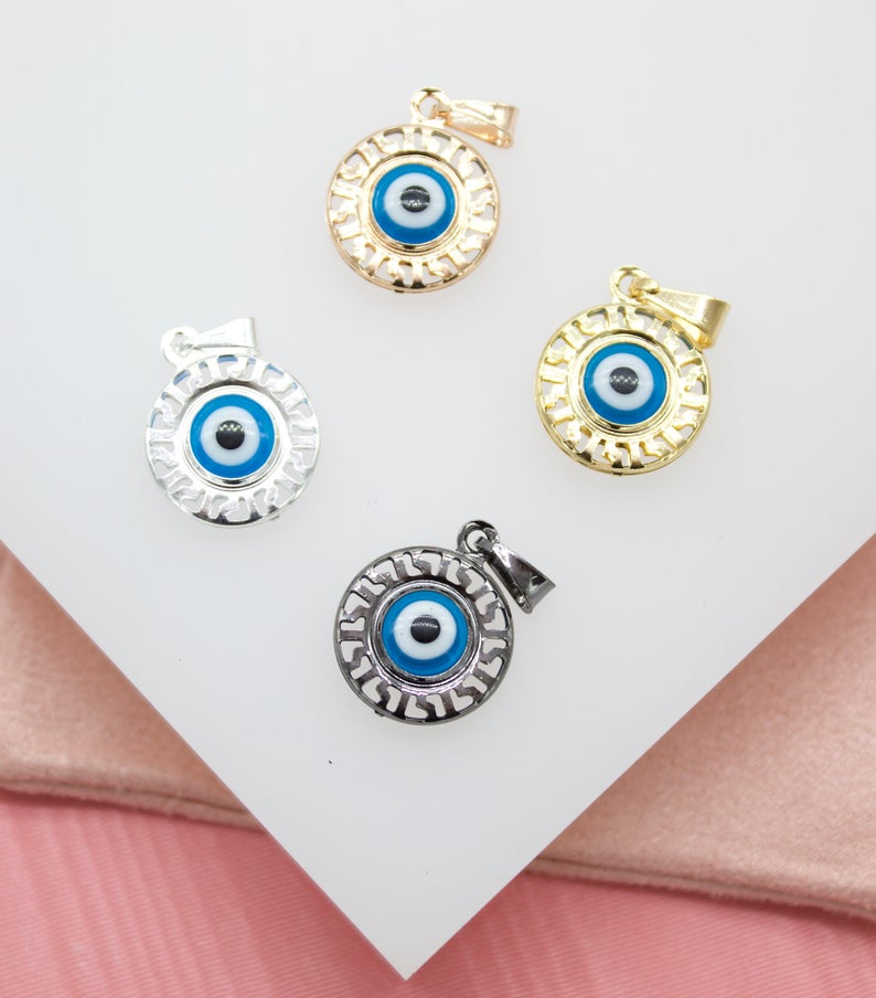 Four round evil eye pendants in gold, silver, and black metal finishes rest on a white surface.
