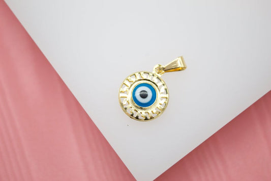 A gold evil eye pendant rests on a white display surface against a pink background.