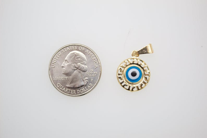A small gold evil eye pendant rests next to a US quarter coin for scale.