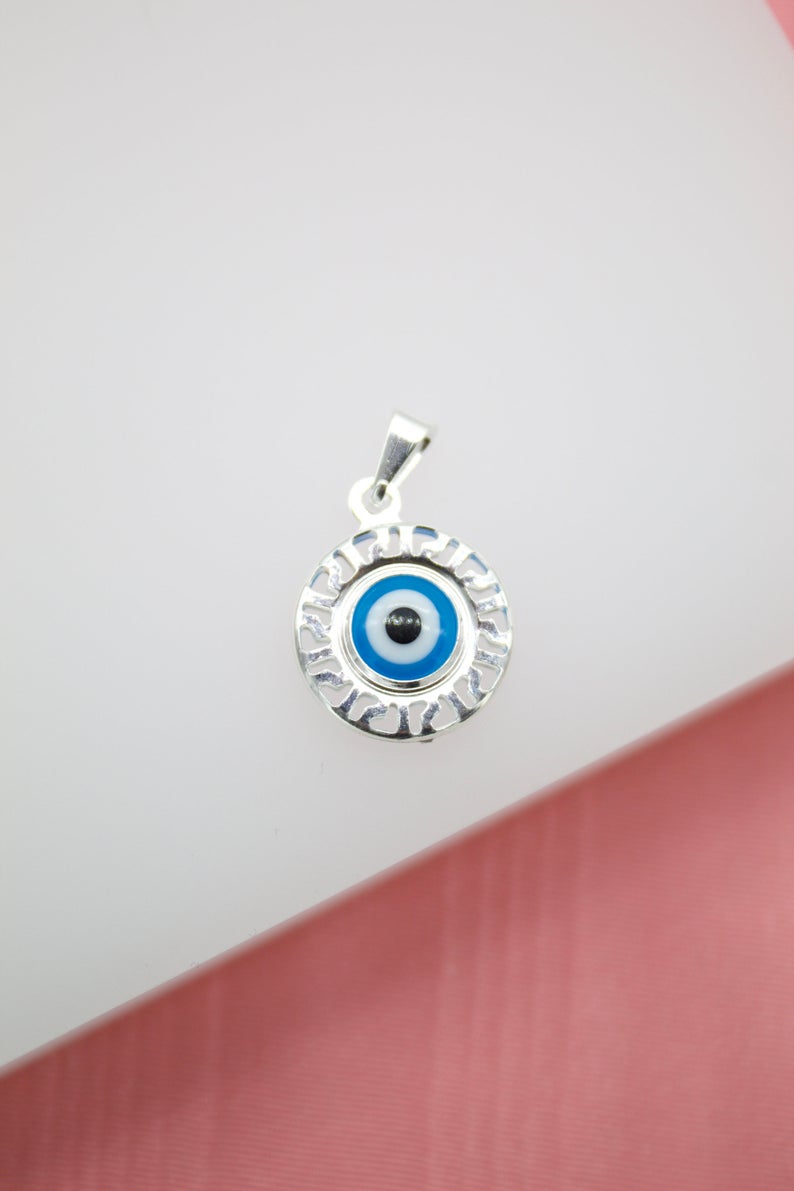 A silver evil eye pendant features a blue and white glass amulet surrounded by an ornate frame.