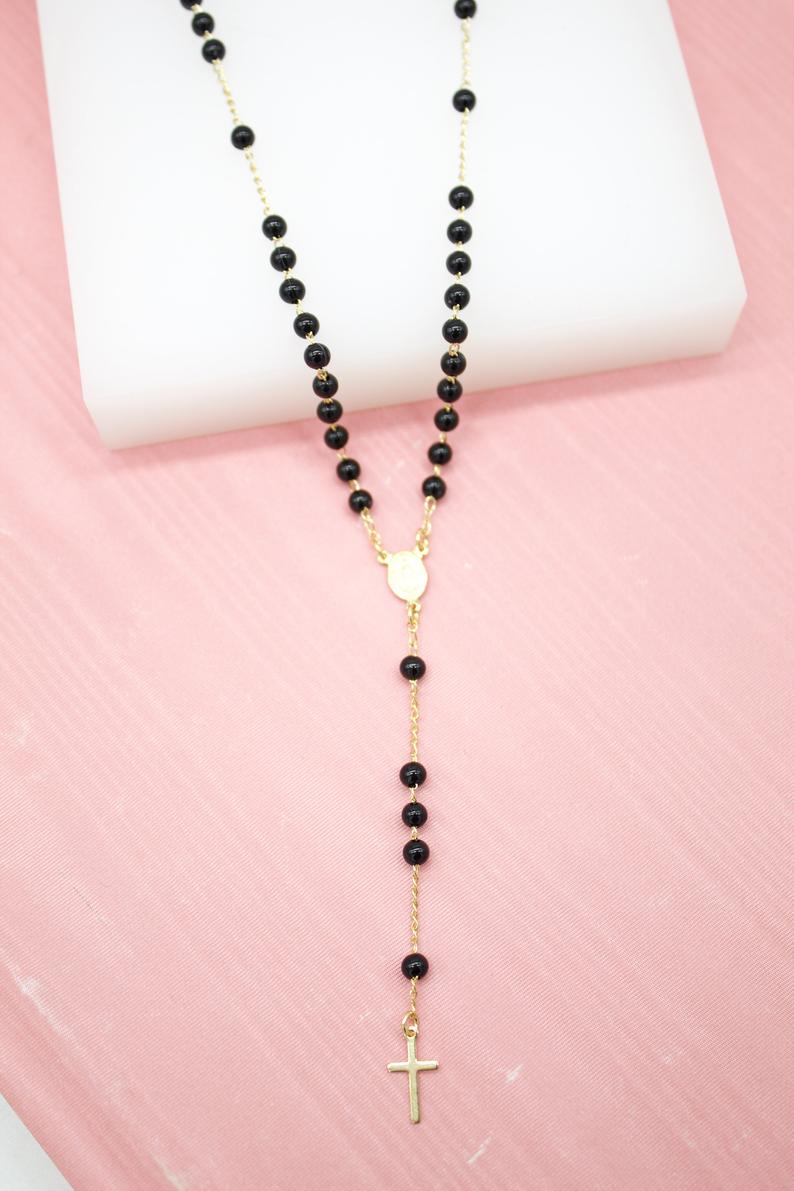 A gold rosary necklace featuring shiny black beads rests gracefully against a light pink background.