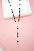 A gold rosary necklace featuring shiny black beads rests gracefully against a light pink background.