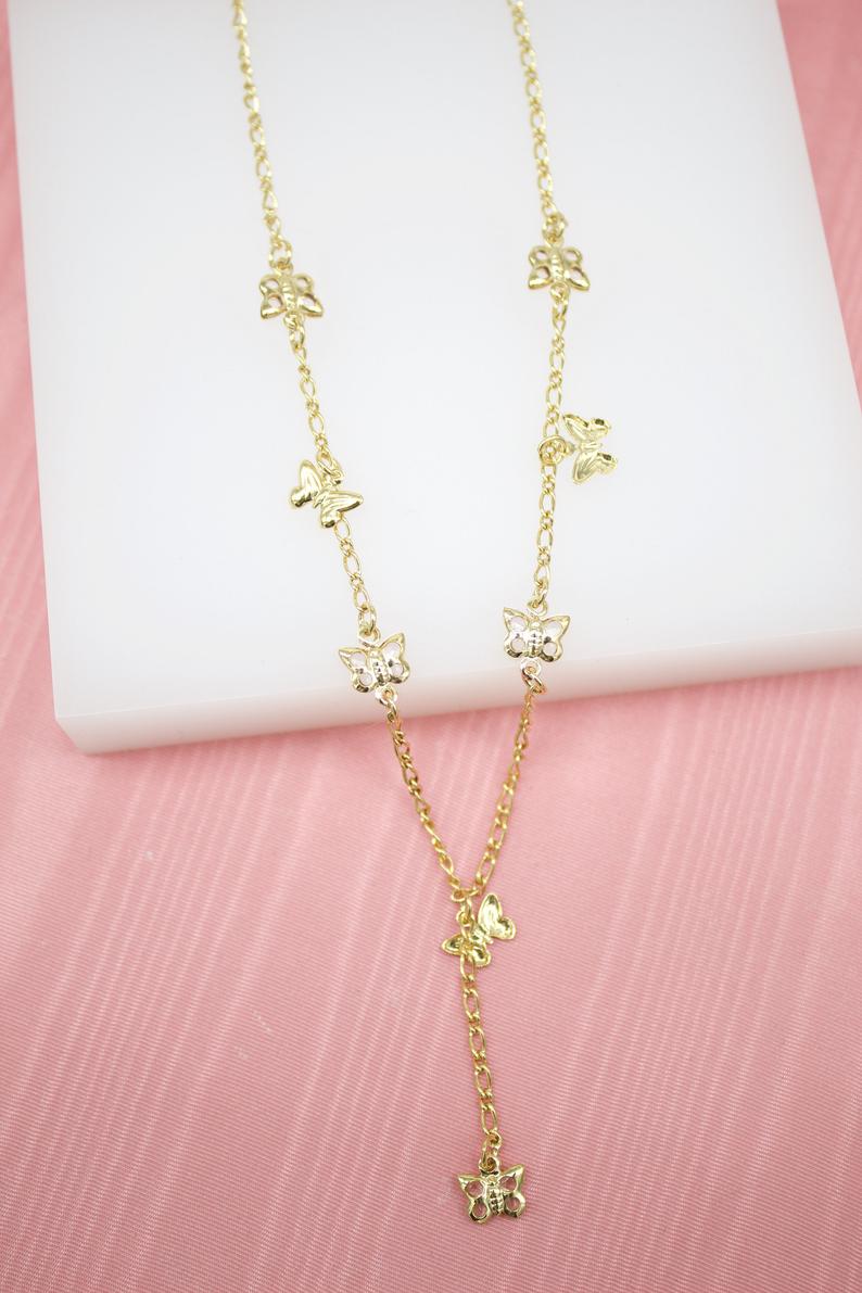 A delicate gold butterfly lariat necklace rests on a white display block against a soft pink background.