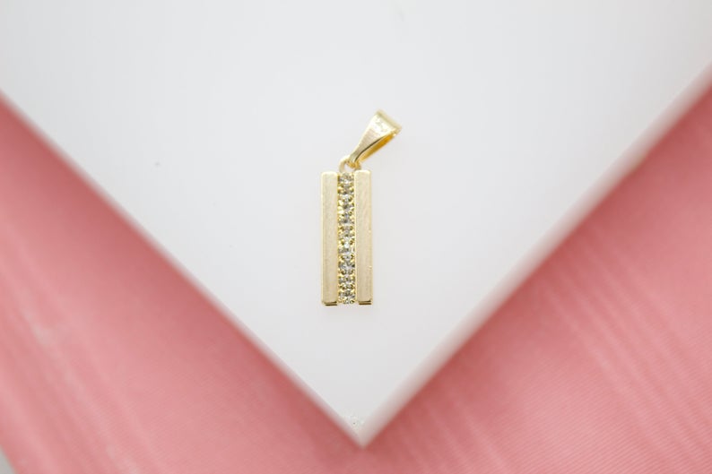 A gold rectangular pendant featuring a vertical row of sparkling cubic zirconia stones rests on a white display surface.