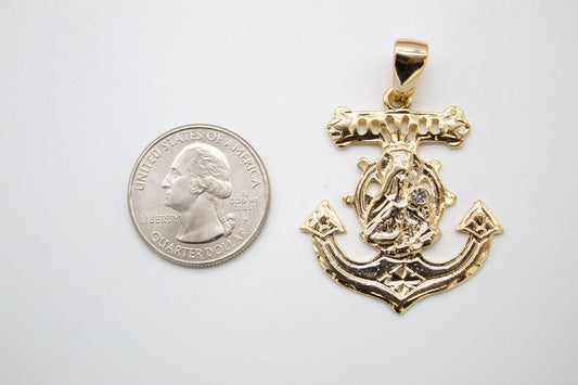 A gold anchor pendant featuring a religious figure at the center rests next to a US quarter coin for scale.