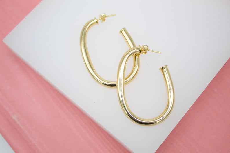 A pair of sleek, polished gold oval hoop earrings rests on a white display surface.