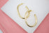 A pair of sleek, polished gold oval hoop earrings rests on a white display surface.