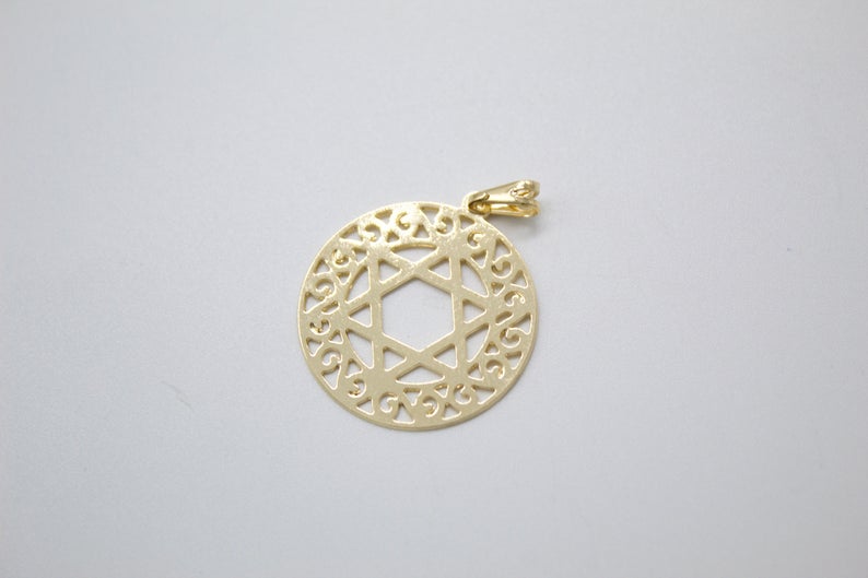 A gold pendant featuring a Star of David inside an intricate circular filigree border rests on a light gray surface.