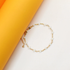 A delicate gold chain bracelet features small white beads arranged symmetrically against a bright yellow and white background.