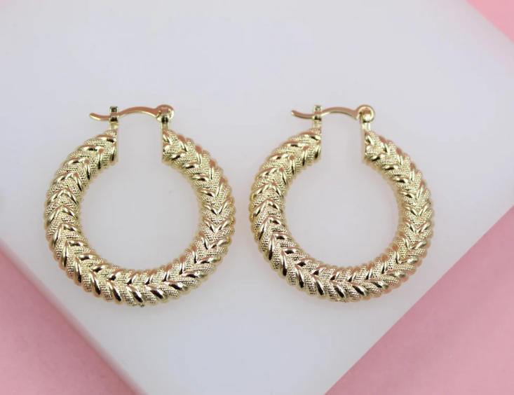 A pair of textured gold hoop earrings rests on a light display stand.