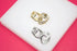 A pair of gold and silver heart-shaped hoop earrings rests on a white display surface against a bright pink background.