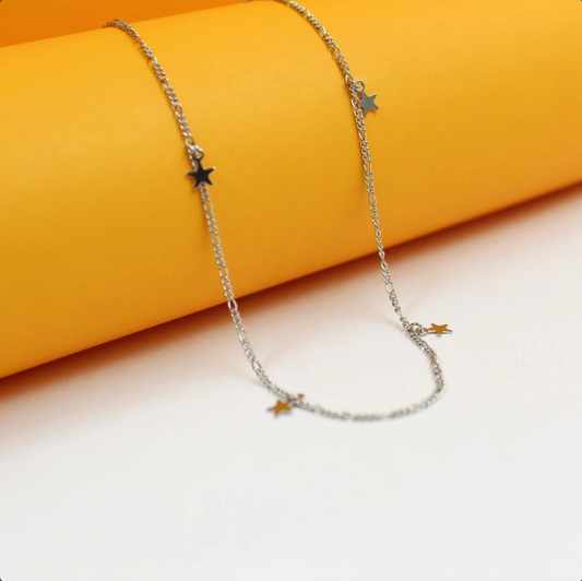 A delicate silver chain necklace featuring multiple small star charms rests against a vibrant yellow and white background.