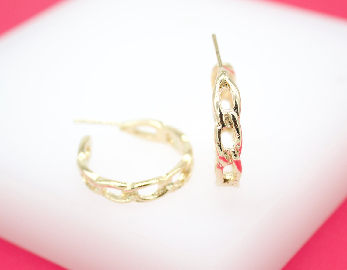 A pair of gold chain-link hoop earrings rests on a white display surface.
