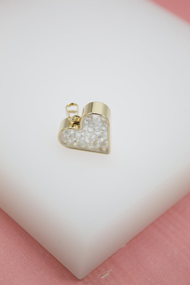 A gold-framed heart-shaped pendant filled with sparkling crystals rests on a white display block.