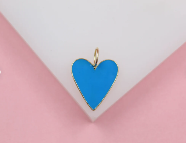 A vibrant blue enamel heart charm with a gold border rests on a white and pink surface.