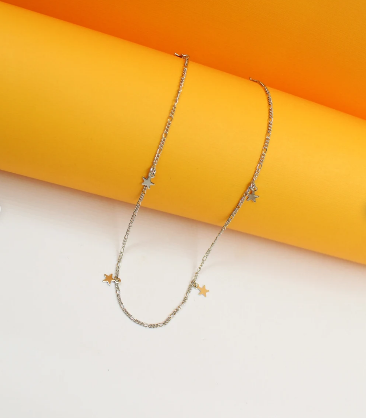 A delicate silver chain necklace featuring multiple dangling star charms rests against a vibrant yellow and white background.