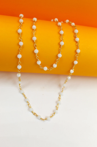 A delicate gold chain necklace featuring alternating white beads drapes gracefully over a vibrant orange and white background.