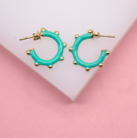 A pair of vibrant turquoise hoop earrings featuring textured gold studs rests on a light pink and white background.