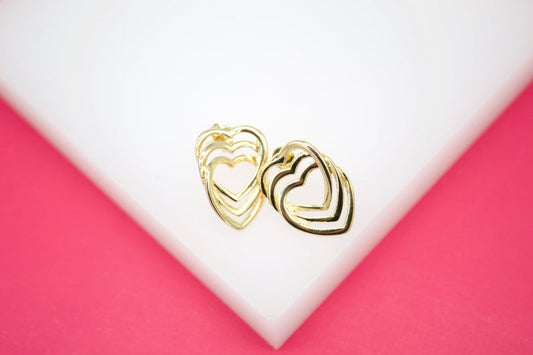 A pair of gold multi-heart stud earrings rests on a white display surface against a pink background.