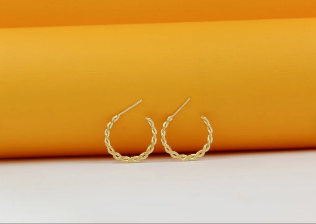 A pair of elegant twisted gold hoop earrings rests against a vibrant orange and white background.