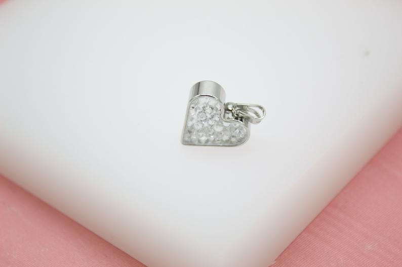 A silver heart pendant filled with sparkling crystals rests against a white and pink background.