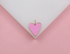 A delicate pink enamel heart pendant rests gracefully against a white and pink background.