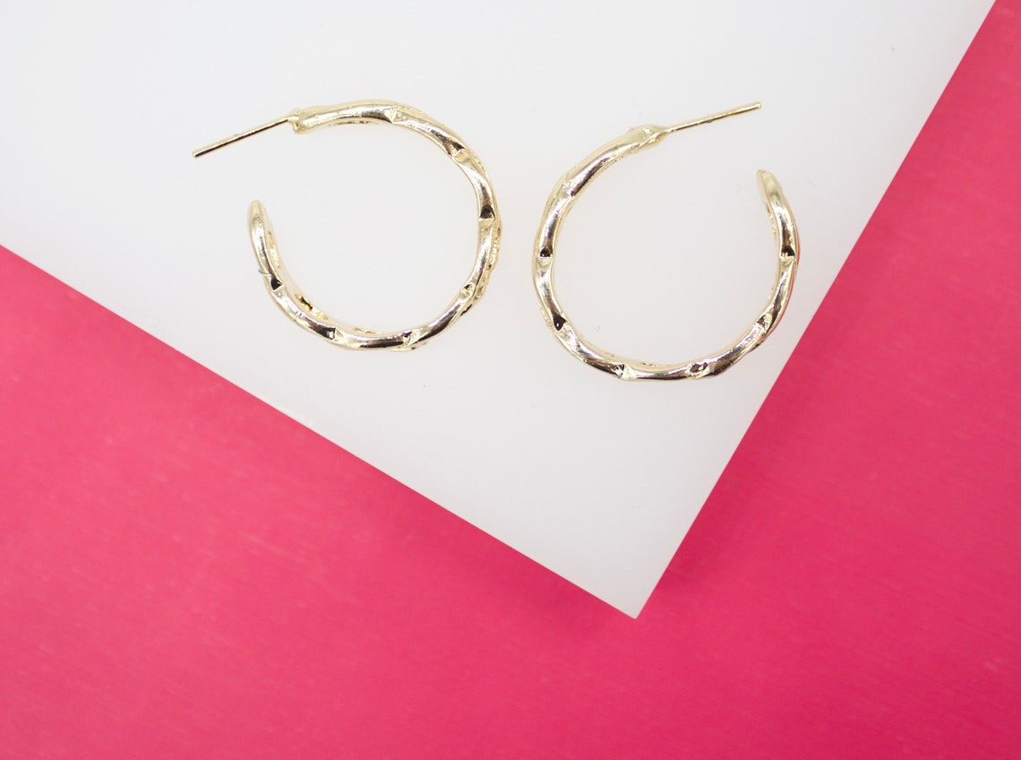 A pair of textured gold hoop earrings rests on a white and pink background.