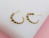 A pair of gold beaded hoop earrings rests on a white display surface.