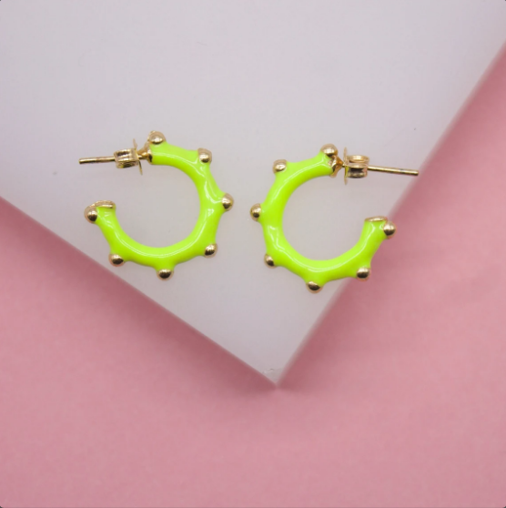 A pair of vibrant neon green hoop earrings featuring delicate gold studs rests on a white and pink display.
