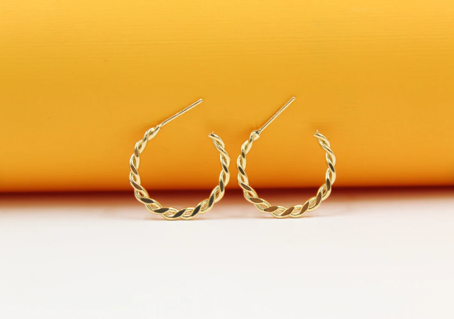 A pair of polished gold twist hoop earrings rests against a vibrant yellow and white background.