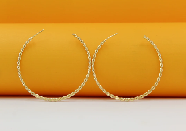 A pair of textured gold hoop earrings rests against a bright yellow background.