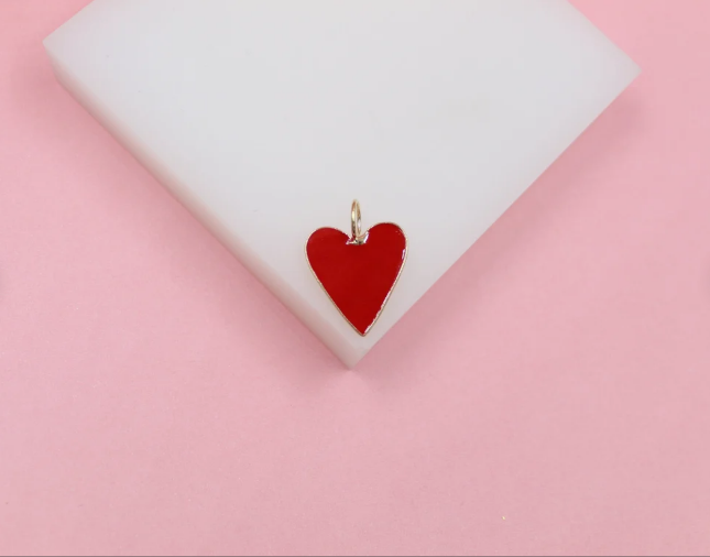 A glossy red enamel heart charm rests on a white display block against a soft pink background.